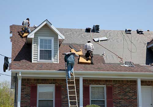 Workers installing new rust-colored shingles on a residential roof