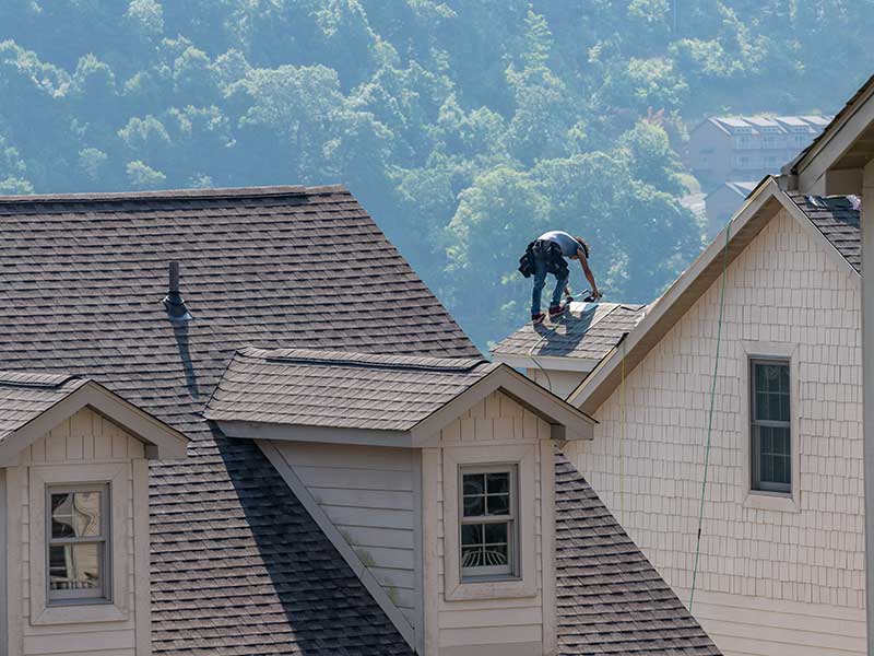 A worker installing the last brown shingles on a large residential roof