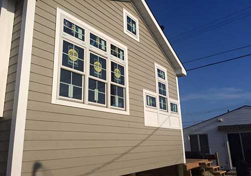 Side view of a home with light brown siding and new Pella windows installed by Quality A+ Home Improvements