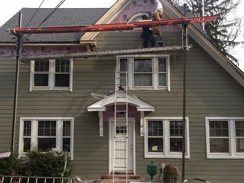 A worker installing the last vinyl light brown-green siding on the front of a home while standing on a platform